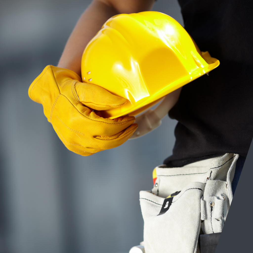 Person wearing work gloves carrying a hard hat.