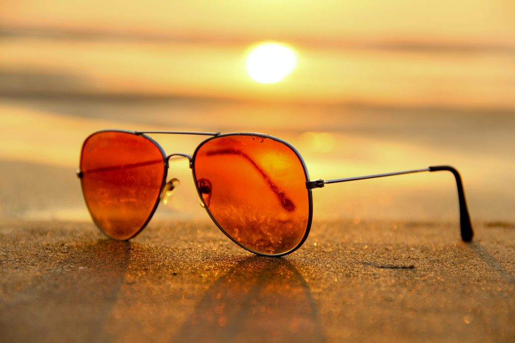Sunglasses on a beach with sun in the background
