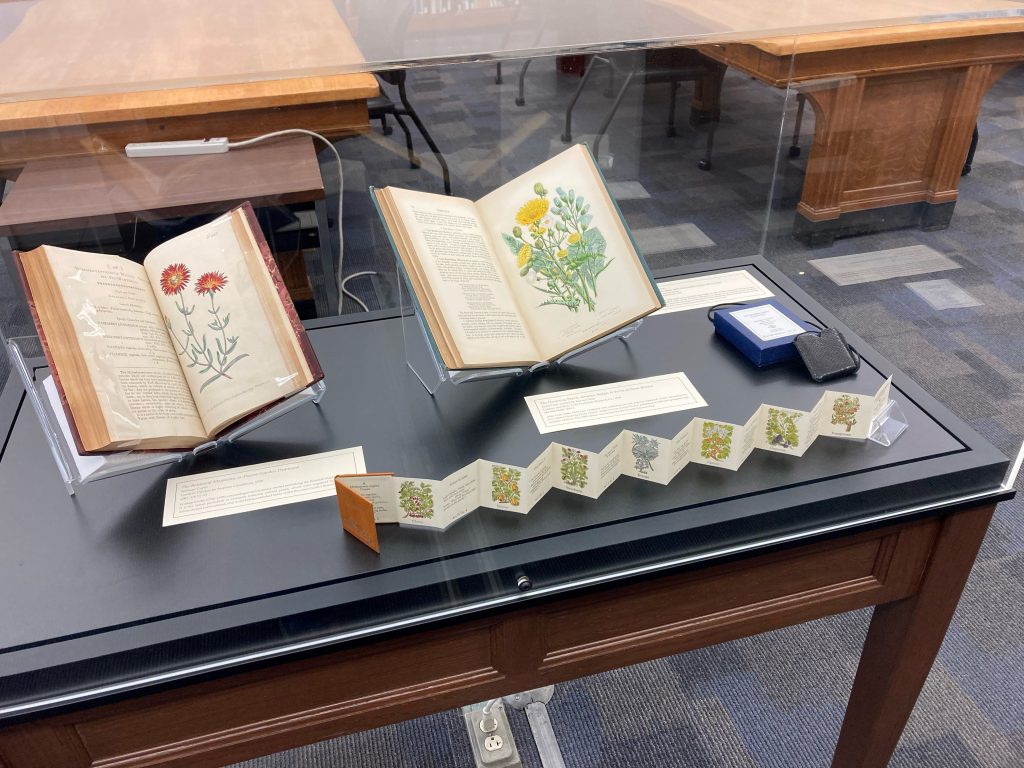 Three books with images of flowers in an exhibit case.