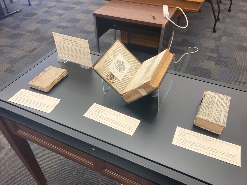 Three books in an exhibit case with labels describing them.