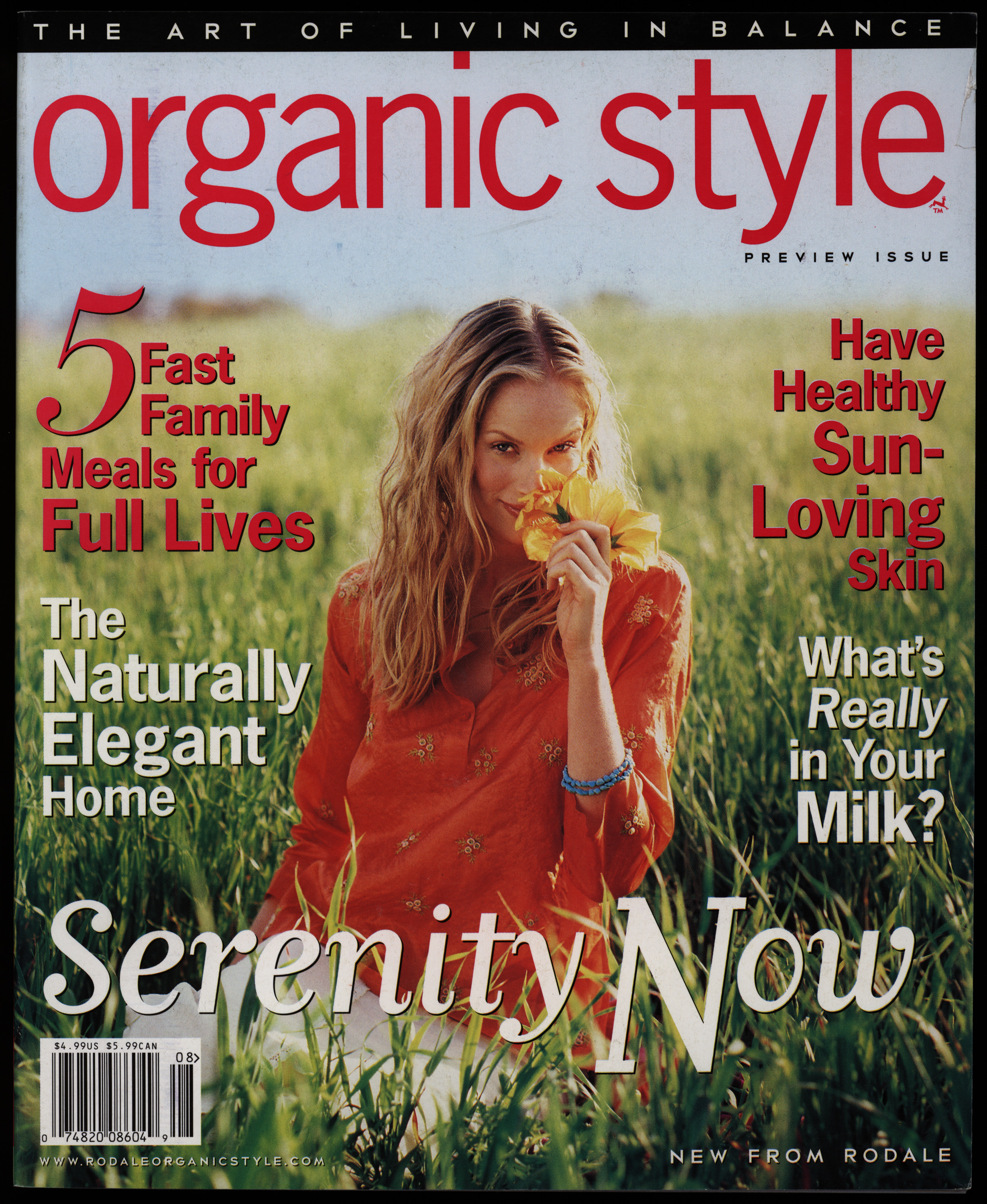 Magazine cover with text in white and red and an image of a woman smelling a flower in a field in the background