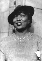 Zora Neale Hurston Portrait. She is wearing a hat and dress, smiling at the camera.